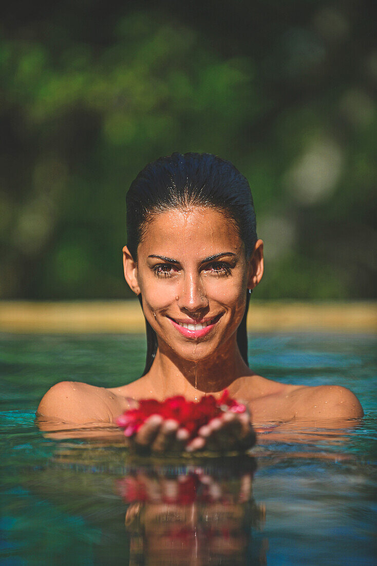 Young attractive woman holding red flowers in an infinity edge swimming pool. The Dutch House, Galle, Sri Lanka