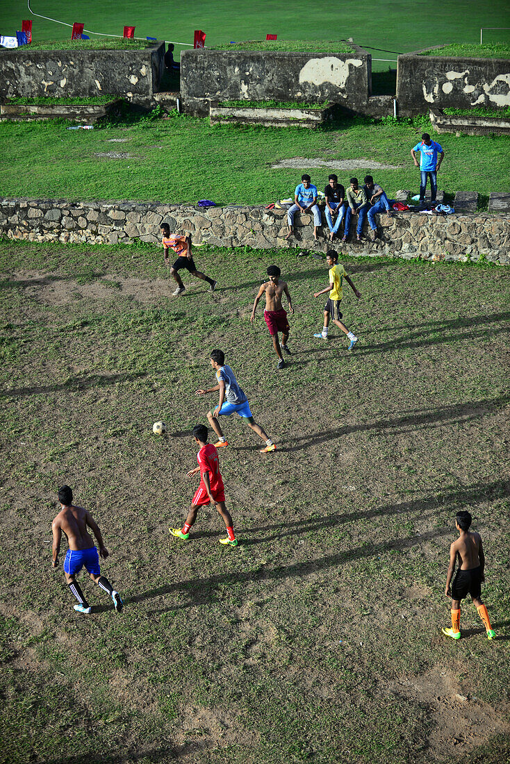 Street soccer game in improvised field next to UNESCO World Heritage, Galle Fort, during Binara Full Moon Poya Day.