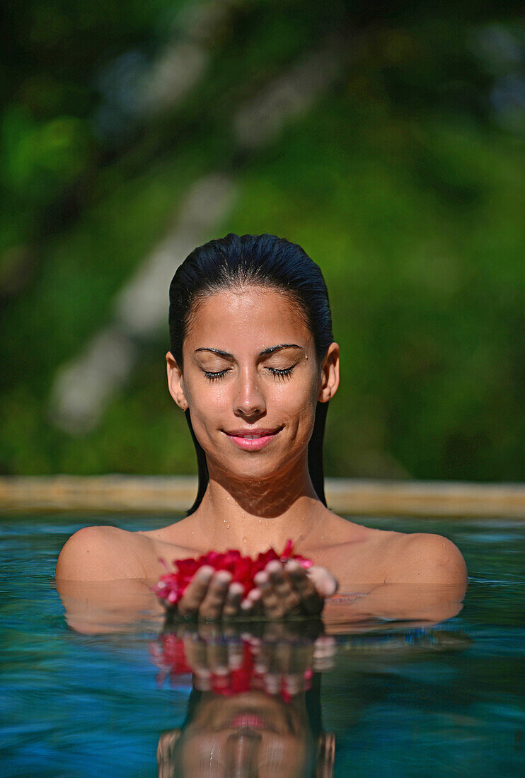 Young attractive woman holding red flowers in an infinity edge swimming pool. The Dutch House, Galle, Sri Lanka