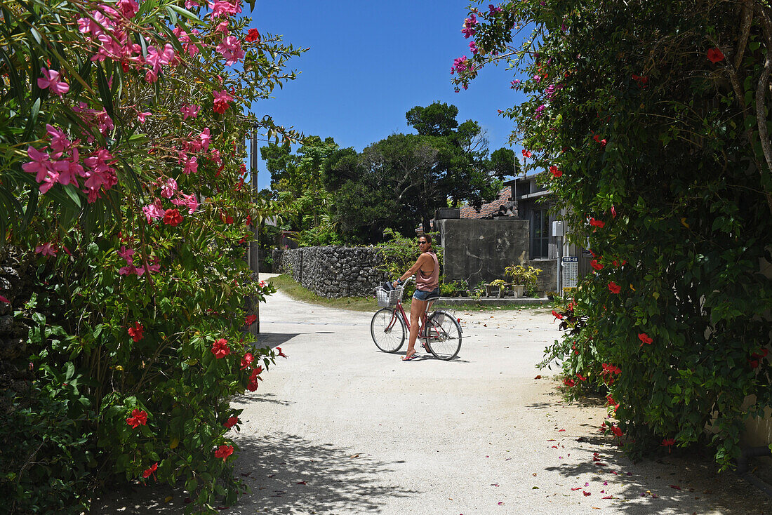 Young woman rides bike in Taketomi Island, Okinawa Prefecture, Japan