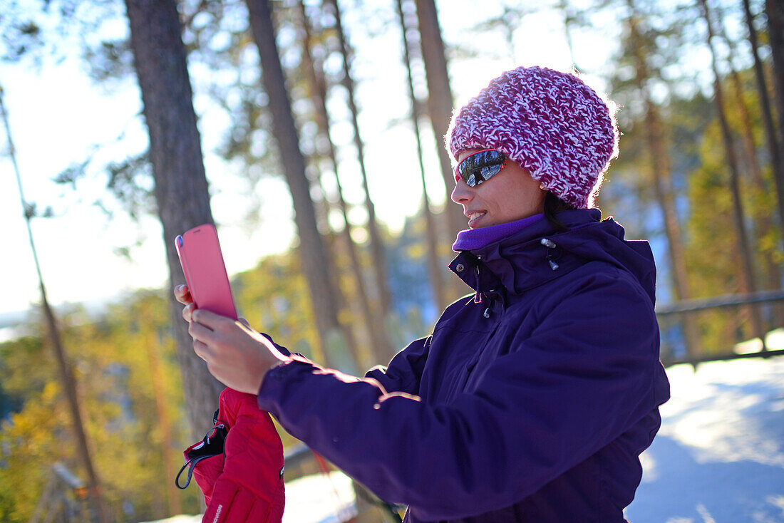 Junge attraktive Frau beim Fotografieren mit dem Mobiltelefon im Skigebiet Pyh? in Lappland