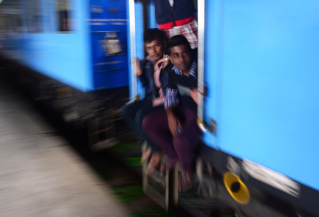 Young men standing by open door. Train ride from Kandy to Nuwara Eliya, Sri Lanka