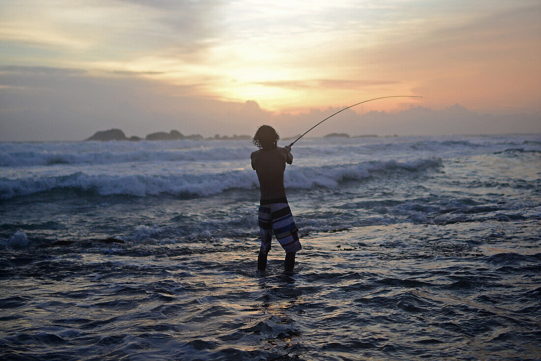Junger Junge beim Fischen am Strand von Hikkaduwa bei Sonnenuntergang, Sri Lanka