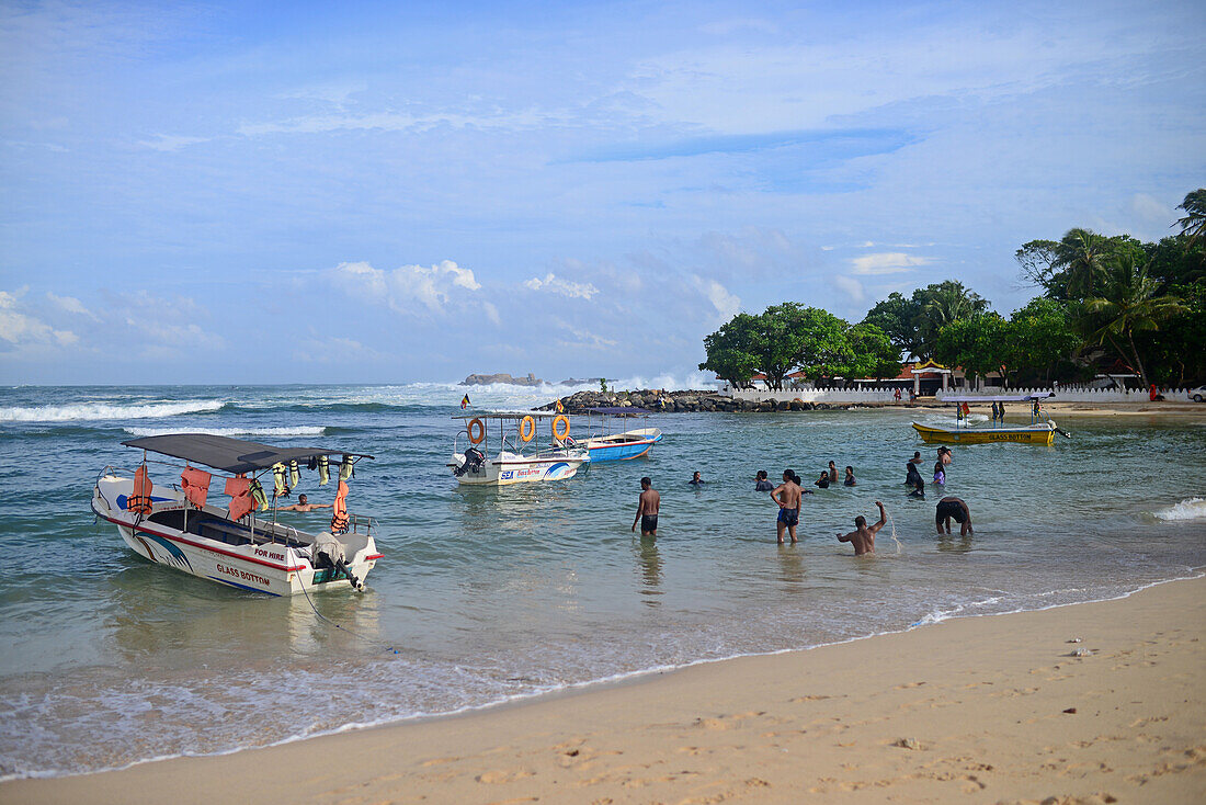 Boot und Menschen im Wasser am Strand von Unawatuna, Sri Lanka
