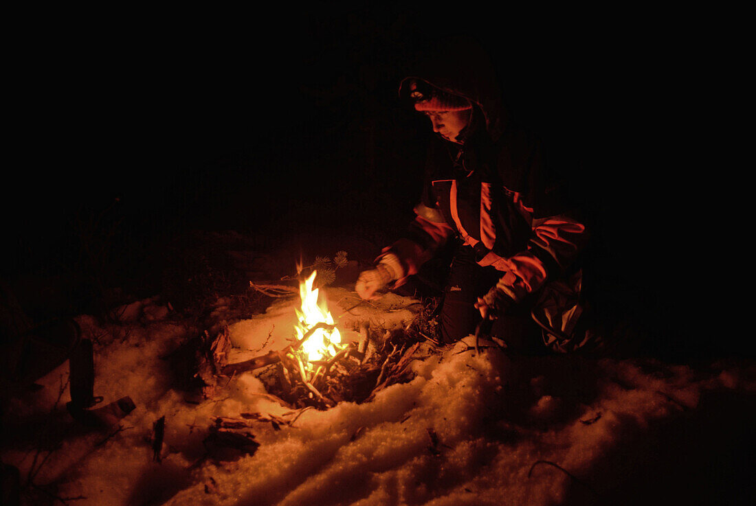 Junge Frau bereitet nachts ein Lagerfeuer im Schnee vor. Inari, Lappland