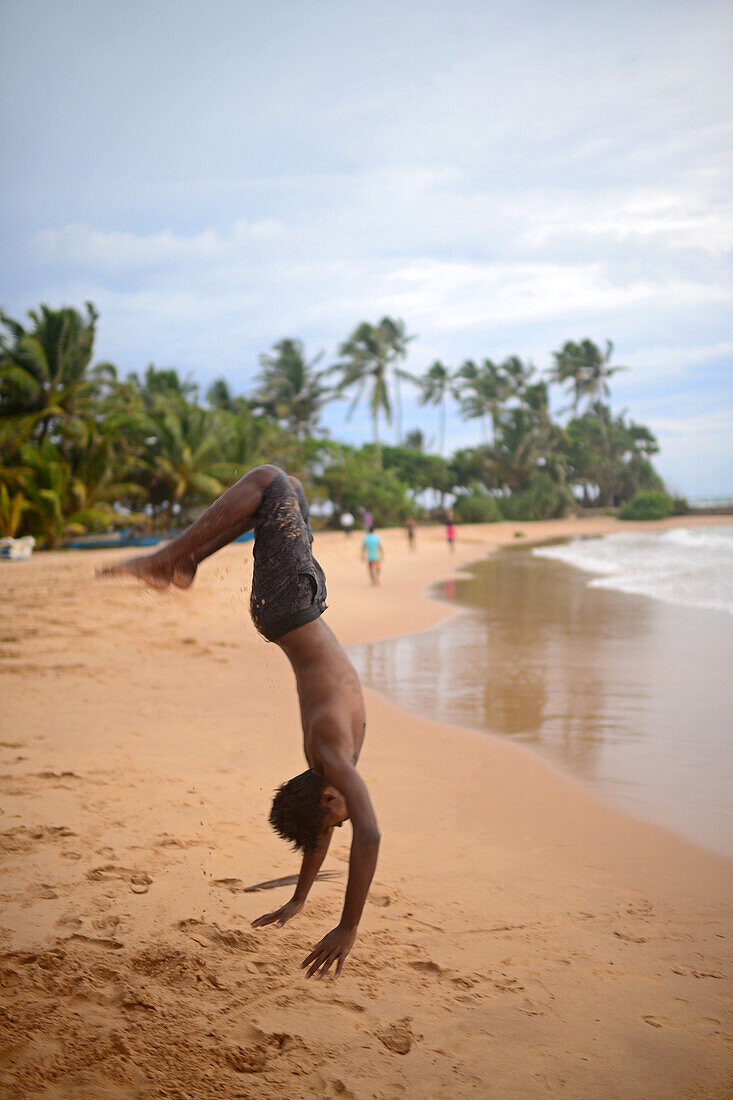 Junger Mann zeigt akrobatische Sprünge am Strand von Hikkaduwa, Sri Lanka