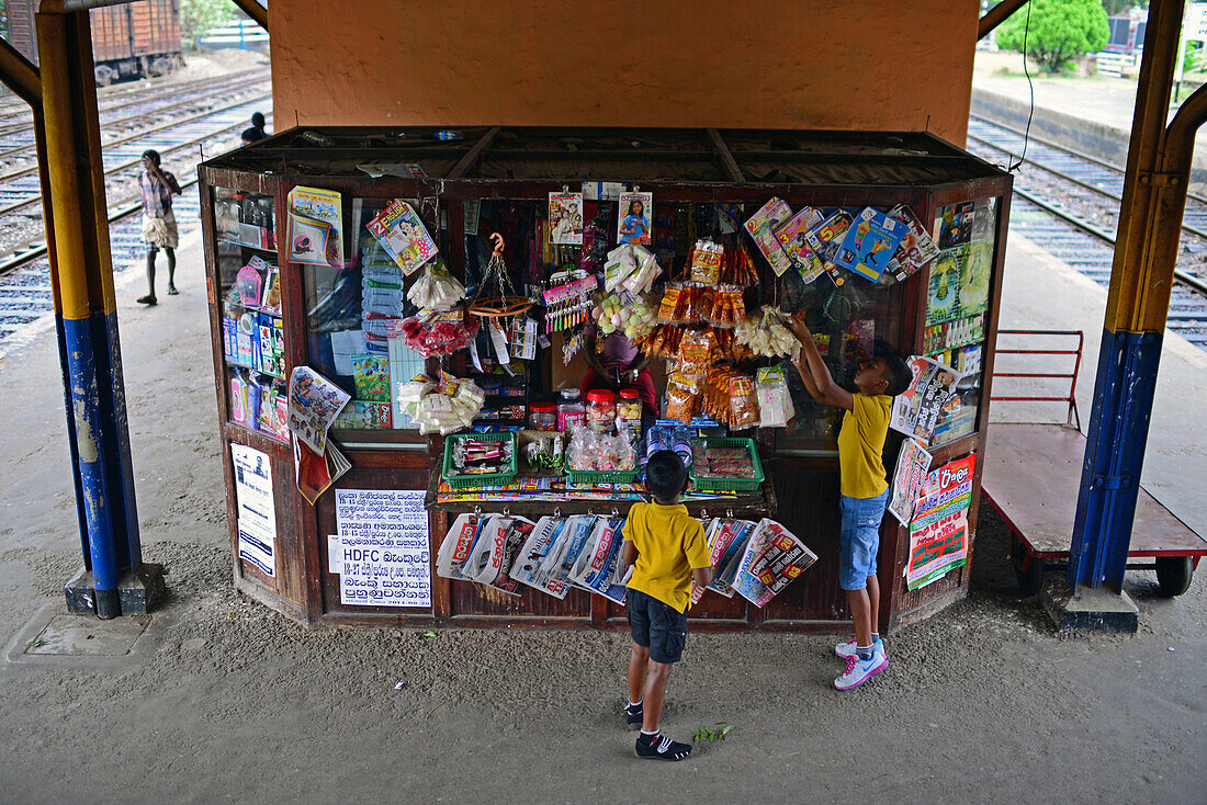 Two kids at food and news stand in train station, Sri Lanka