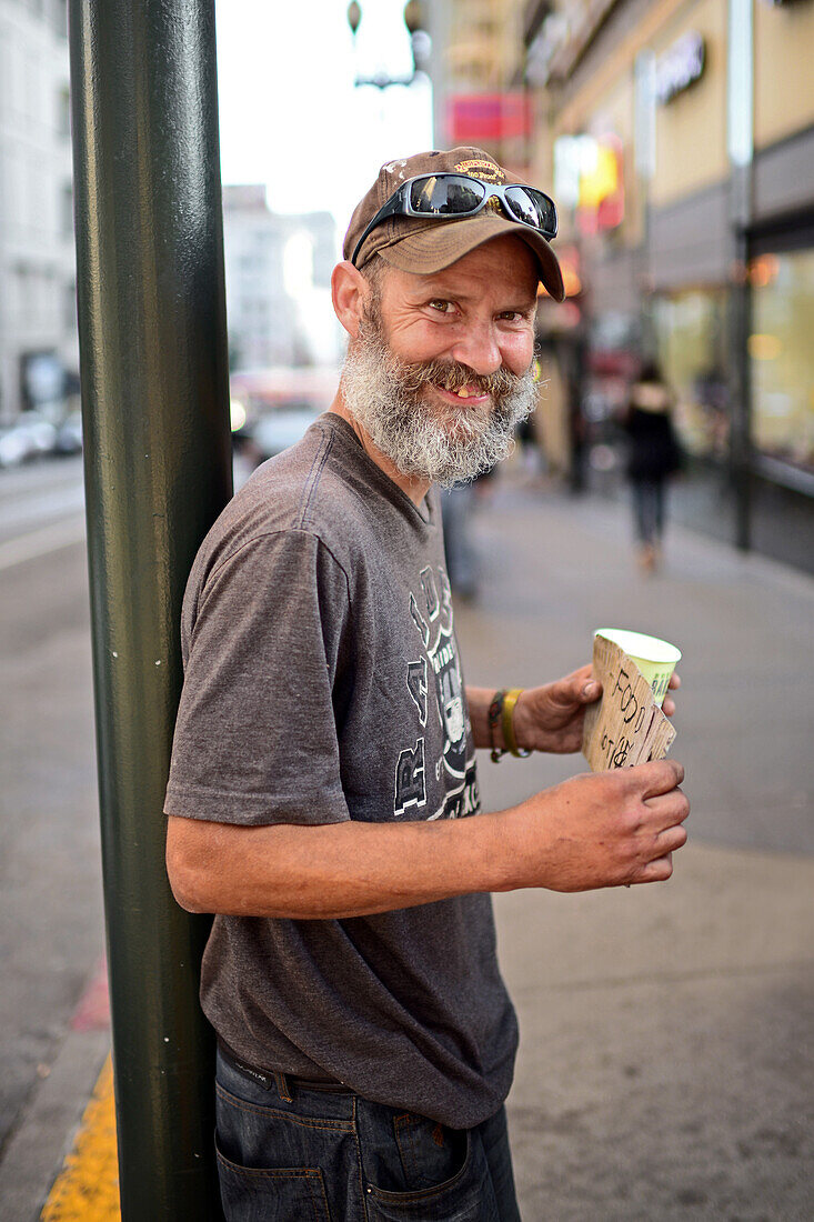 Perrie, kind homeless man from Michigan, poses in the streets of San Francisco with a sign that reads "Smile", California.