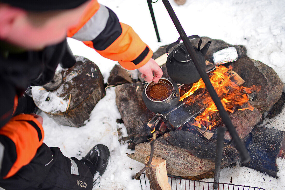 Antti, junger Reiseleiter von VisitInari, bereitet Kaffee und Tee auf einem Feuer in der Wildnis des Inari-Sees, Lappland, Finnland, zu