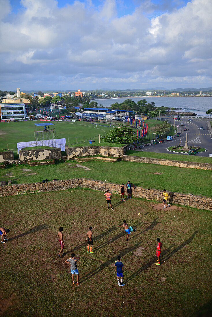 Street soccer game in improvised field next to UNESCO World Heritage, Galle Fort, during Binara Full Moon Poya Day.