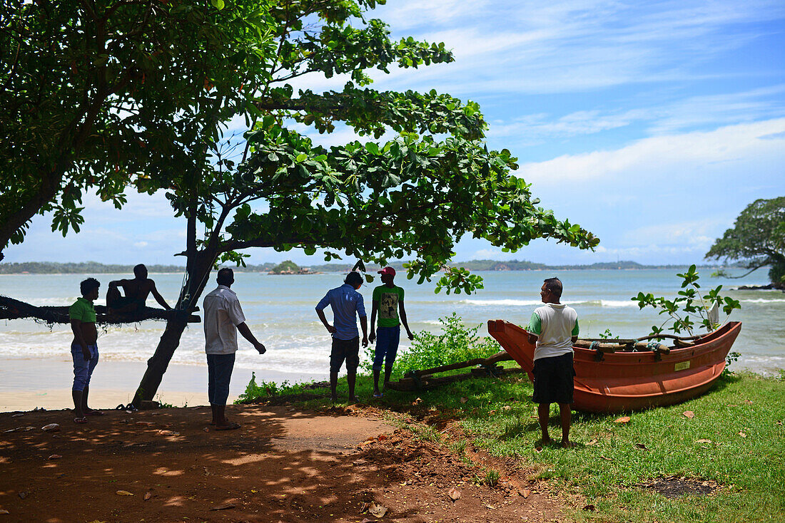 Eine Gruppe von Menschen und ein traditionelles Fischerboot in Weligama, Sri Lanka