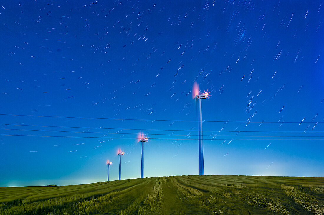 Sternennacht über spanischen Windrädern - Eine faszinierende Langzeitbelichtung, die die ruhige Schönheit von Windrädern vor dem Hintergrund von Sternenspuren am klaren Nachthimmel Spaniens einfängt