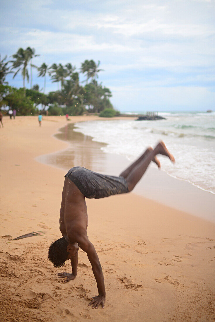 Junger Mann zeigt akrobatische Sprünge am Strand von Hikkaduwa, Sri Lanka
