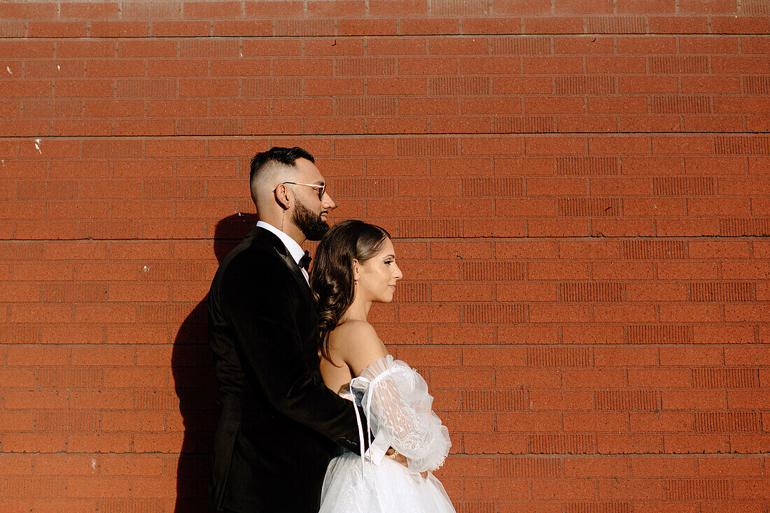 Side view of bride and groom against brick wall