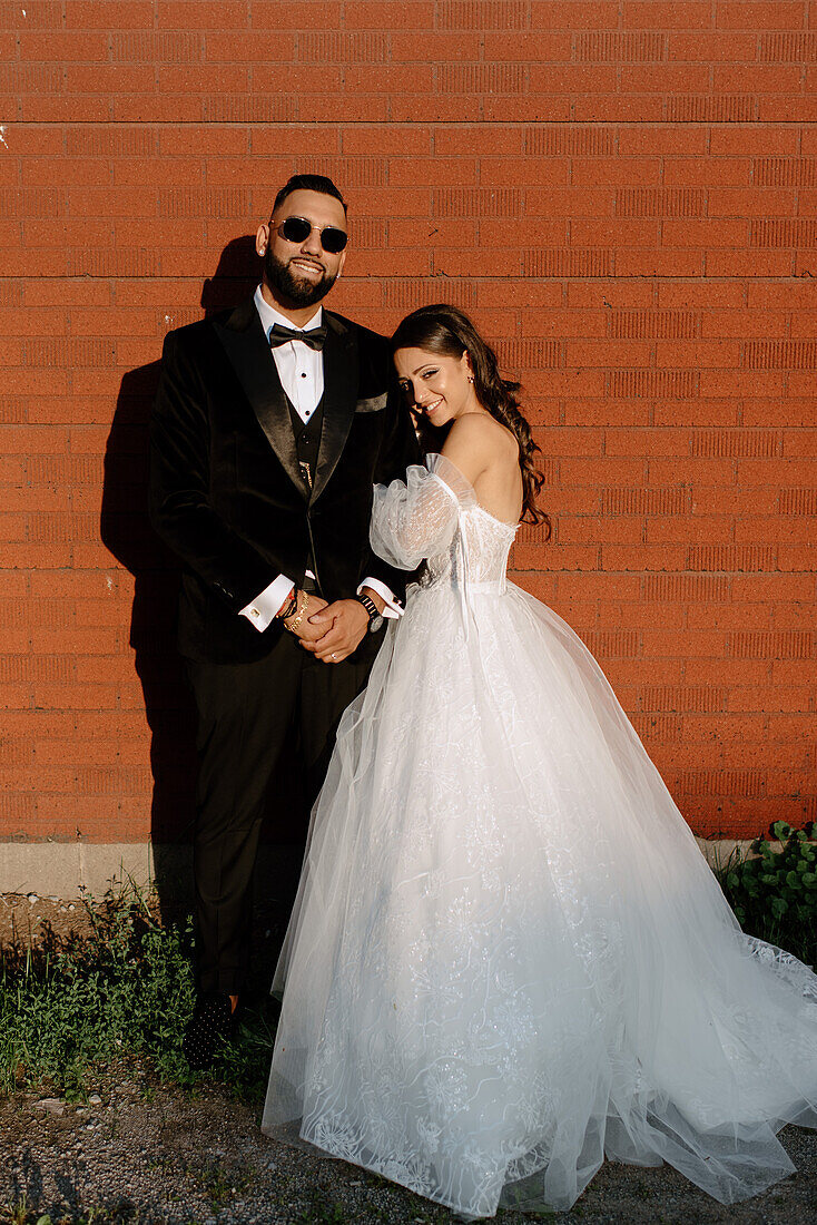 Portrait of bride and groom standing against brick wall
