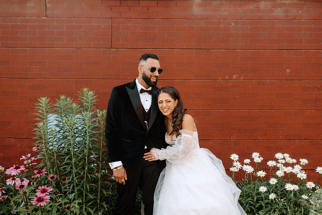 Smiling bride and groom against brick wall and flowers