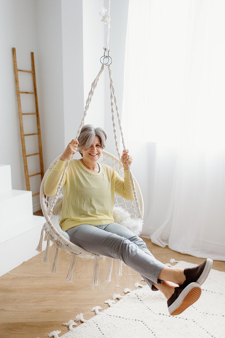 Portrait of smiling woman sitting in swing chair at home