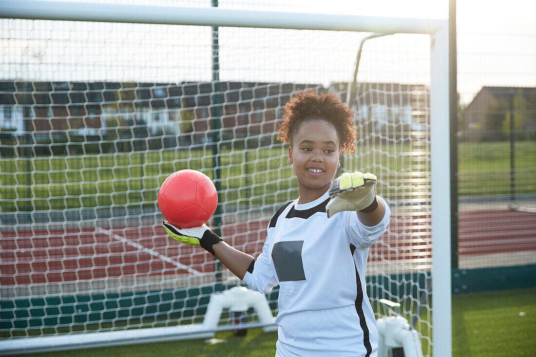 UK, Smiling female soccer goalie (12-13) throwing ball