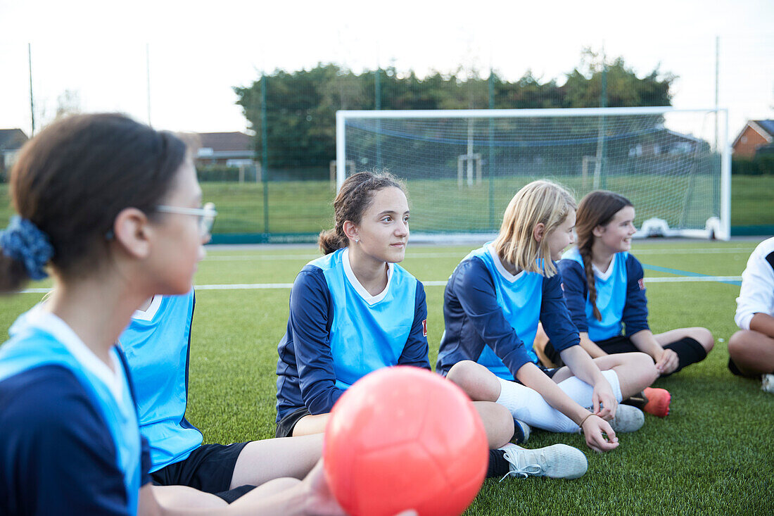 UK, Female soccer team (10-11, 12-13) sitting in field during training