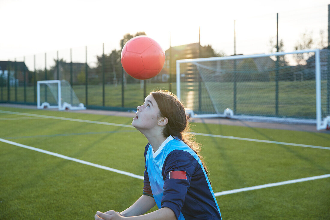 UK, Fußballspielerin (10-11) prellt Ball auf Feld bei Sonnenuntergang