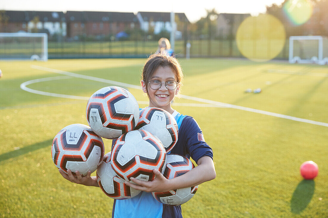 UK, Smiling female soccer player (10-11) holding balls in field