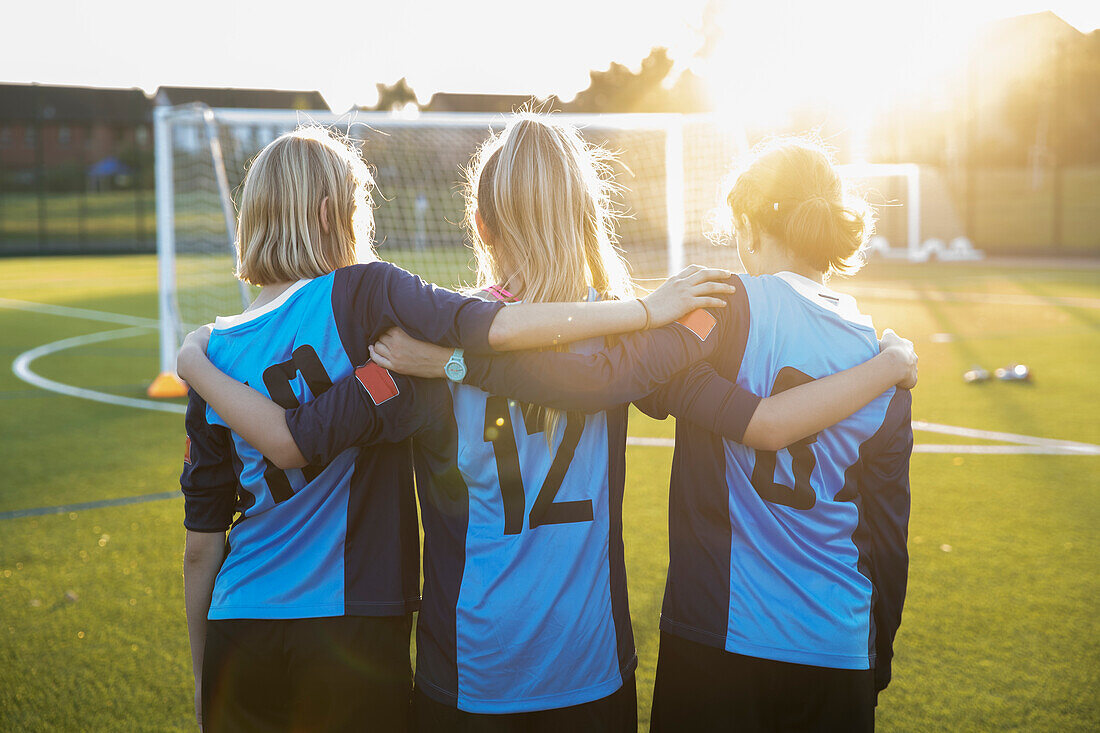 UK, Rückansicht von Fußballspielerinnen (10-11, 12-13), die sich auf dem Feld umarmen