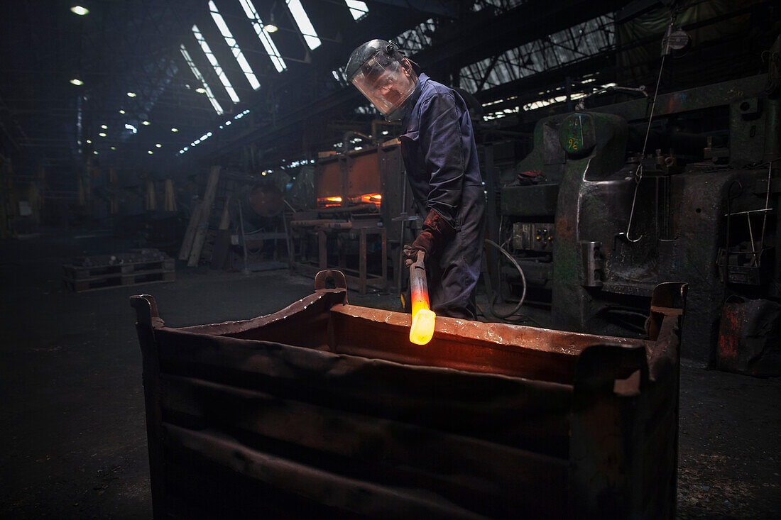 Forge worker preparing to release finished upset forging into steel container