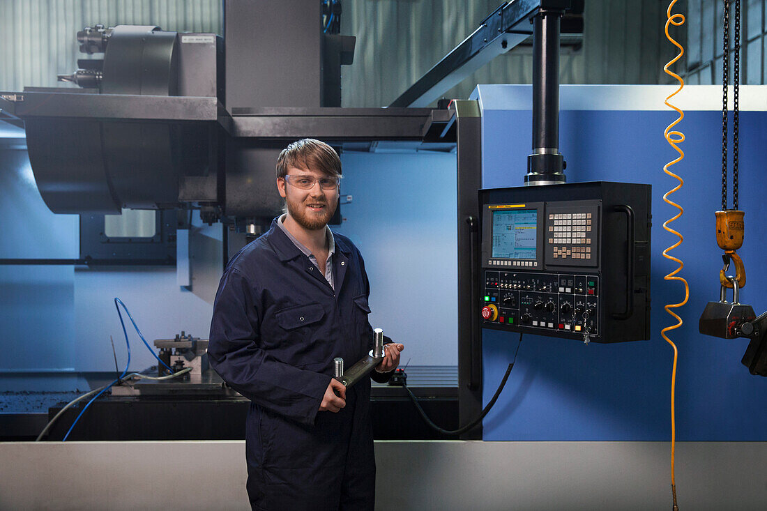 Ein Auszubildender hält ein U-Bolzenband vor einer CNC-Maschine