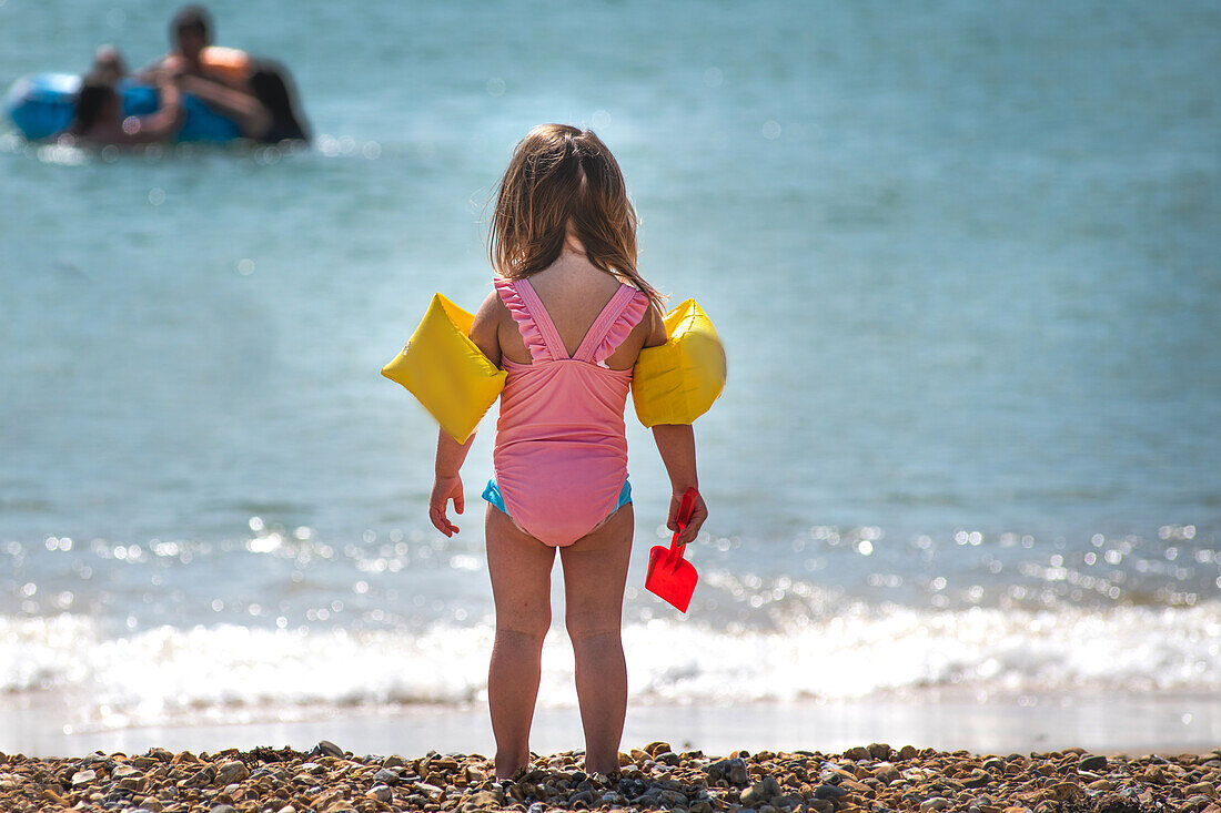 Rückansicht eines Mädchens mit Schwimmflügeln am Strand