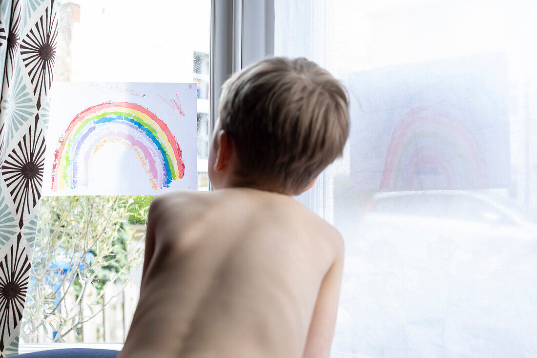 Rückansicht eines hemdlosen Jungen (18-23 Monate), der durch ein Fenster schaut