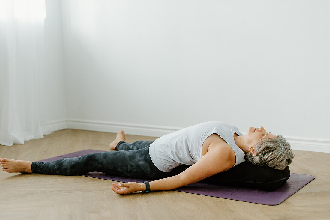 Woman lying on yoga mat at home