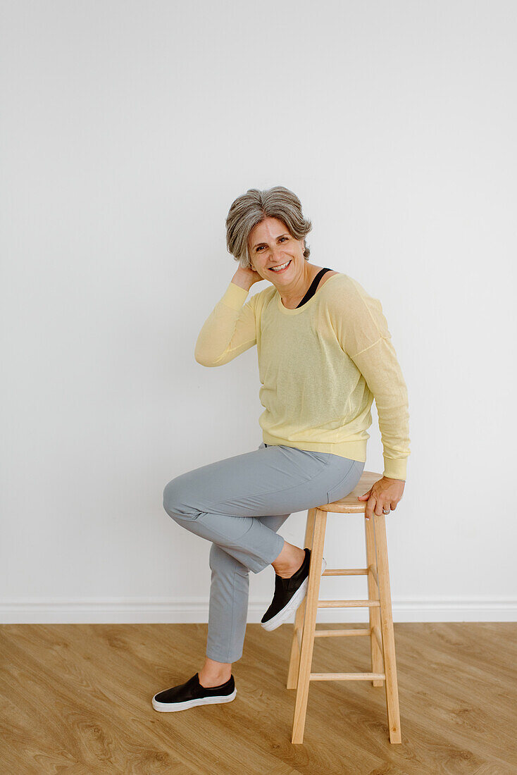 Portrait of smiling woman sitting on stool at home