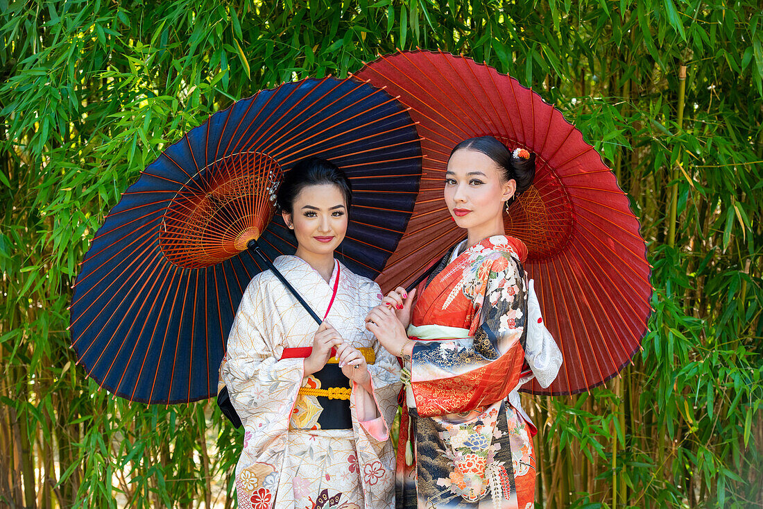 Porträt von zwei Frauen in Kimonos und mit Sonnenschirmen in einem Park