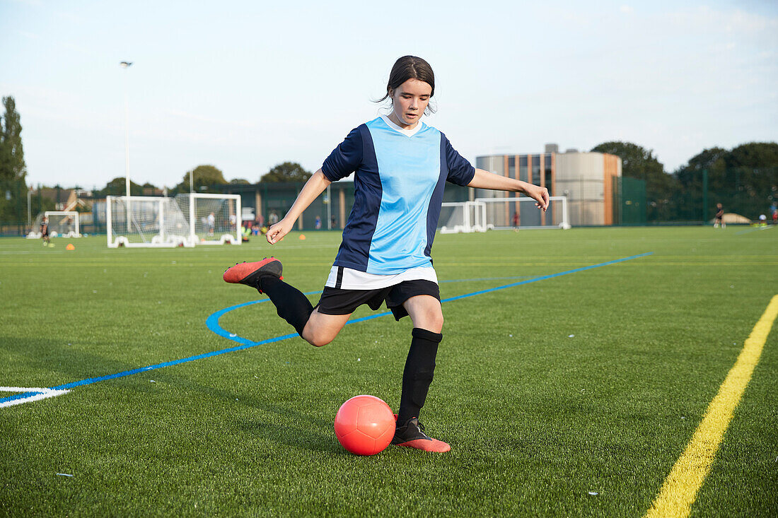 UK, Weibliches Mitglied einer Fußballmannschaft (10-11) kickt Ball auf einem Feld