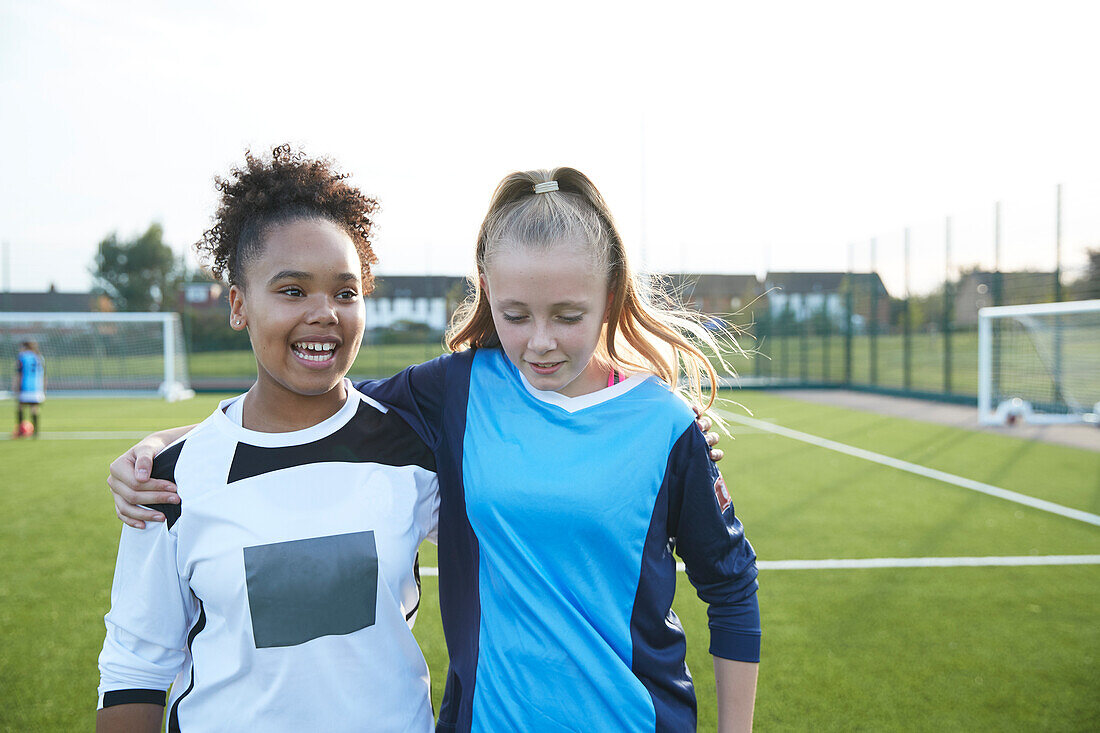 UK, Smiling female soccer team members (12-13) embracing in field