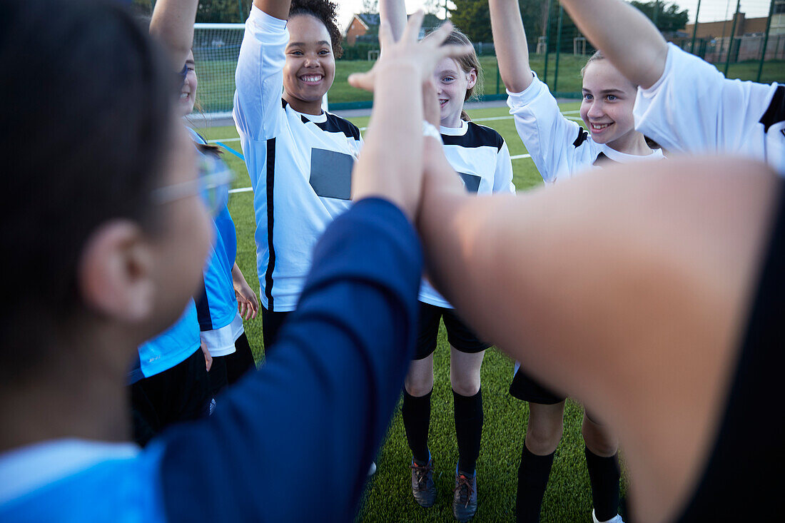 UK, Female soccer team members (10-11, 12-13) raising arms in field