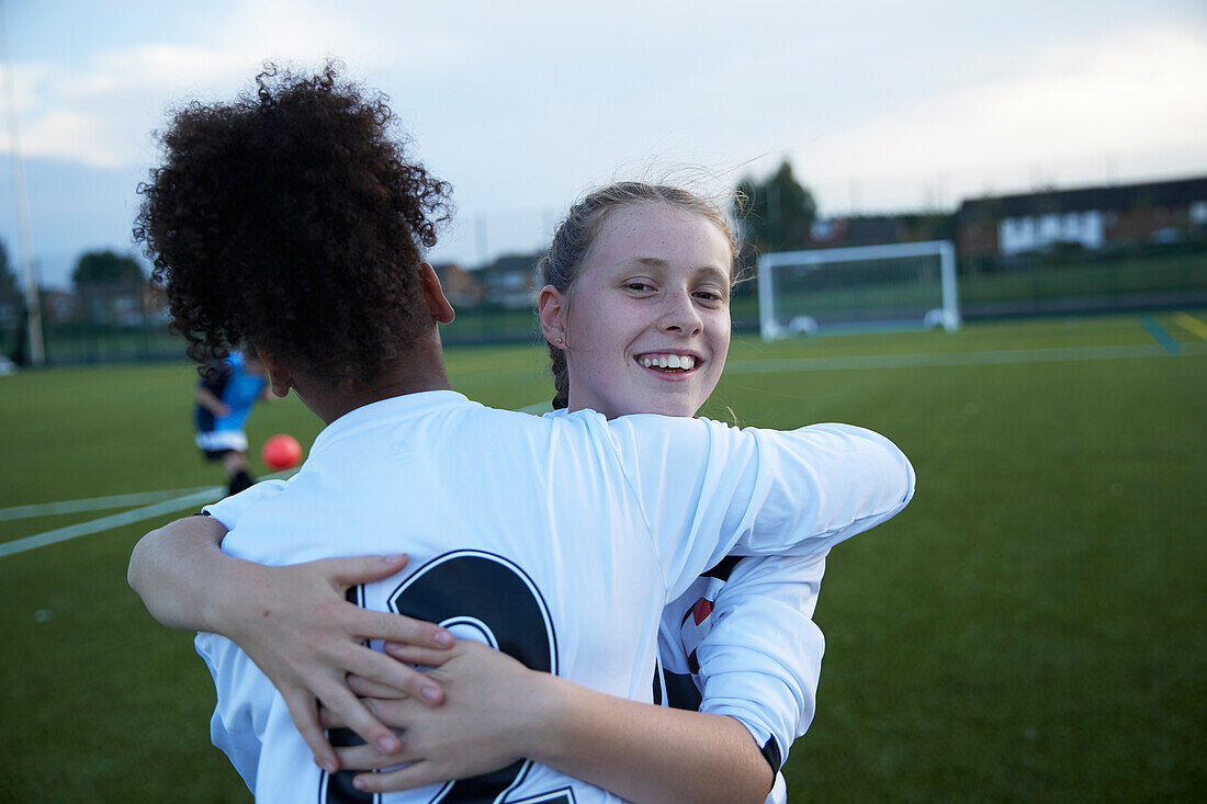 UK, Female soccer team members (10-11, 12-13) embracing in field