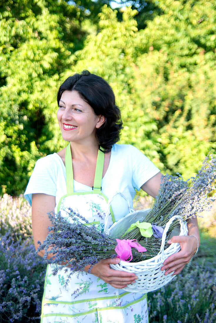 Smiling woman with lavender bunches in basket in field