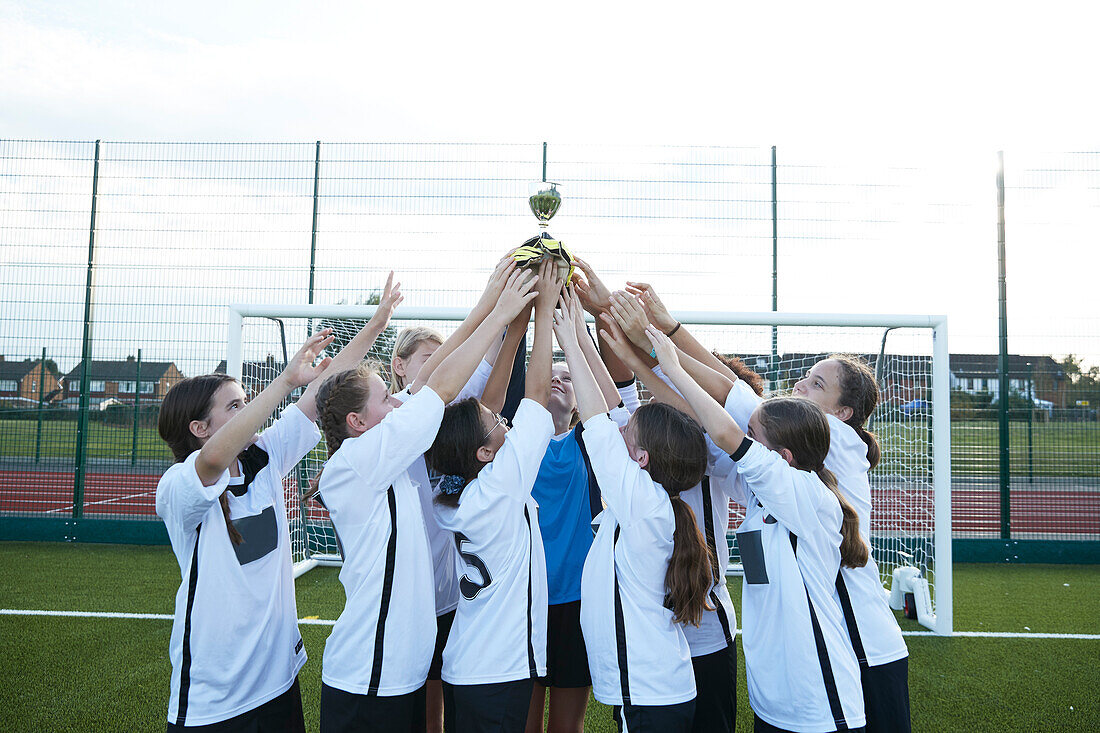 UK, Girls soccer team (10-11, 12-13) holding trophy in soccer field