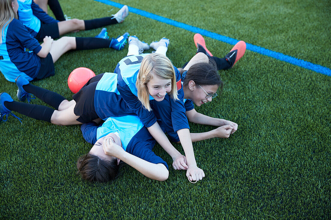 UK, Playful female soccer players (10-11, 12-13) lying in field