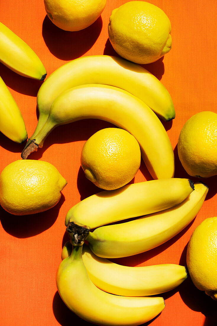 Overhead view of bananas and lemons on orange background