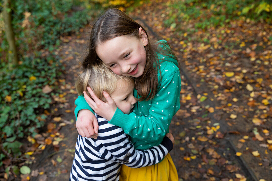 Sister (4-5) and brother (18-23 months) hugging outdoors