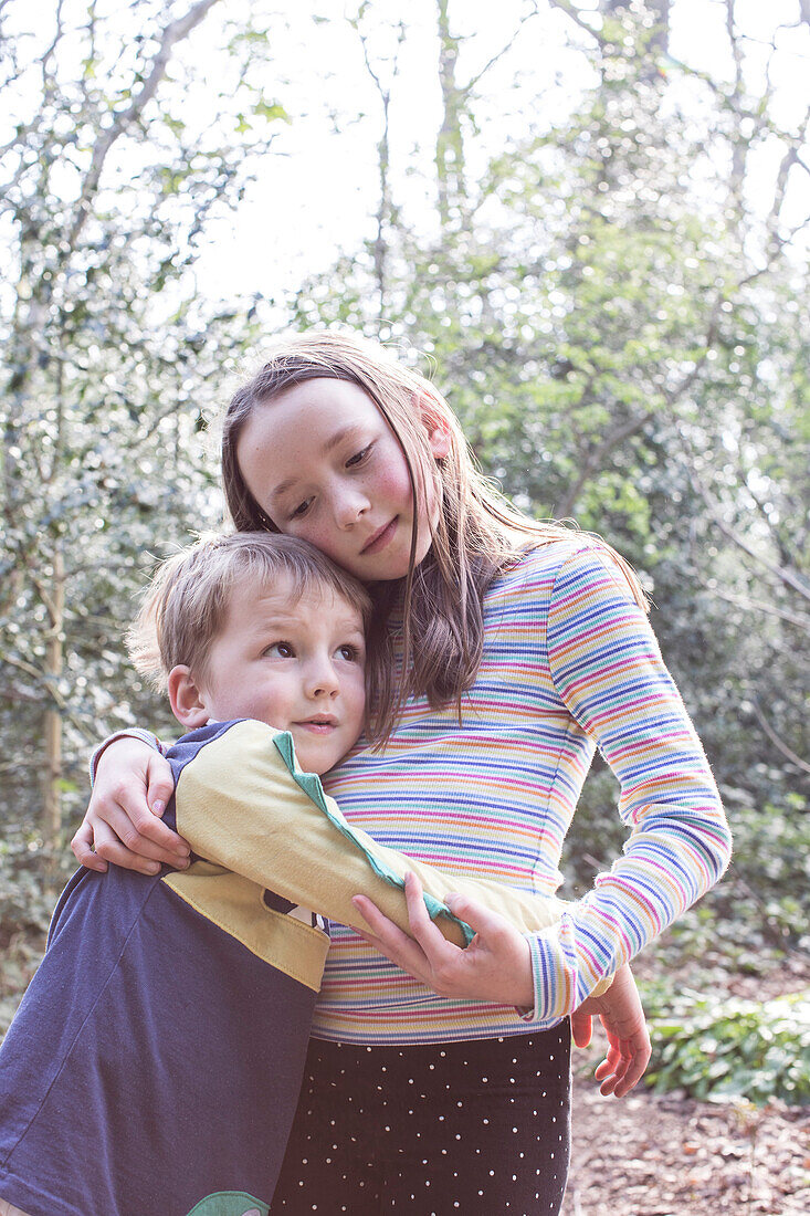 Brother (18-23Êmonths) and sister (4-5) hugging in forest