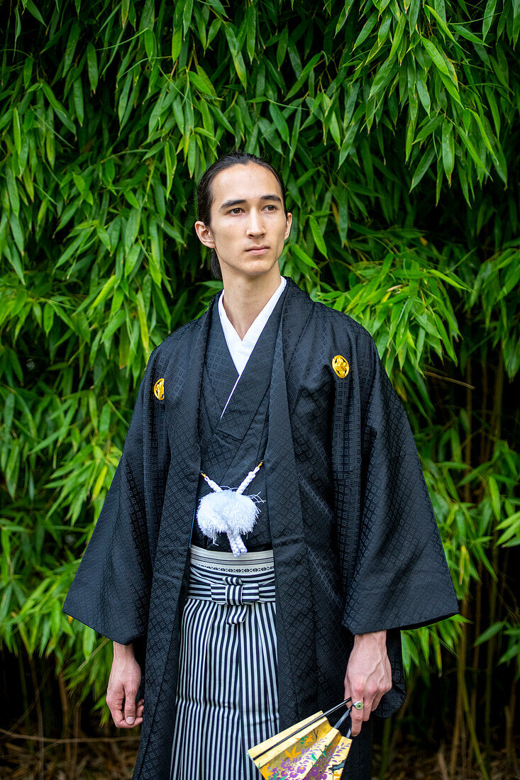 UK, Portrait of young man wearing kimono holding fan in park