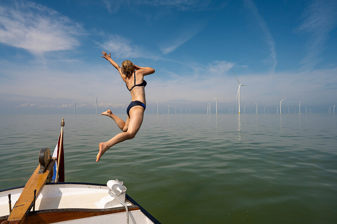 Niederlande, Friesland, Breezanddijk, Mädchen springt in der Nähe von Windkraftanlagen ins Meer