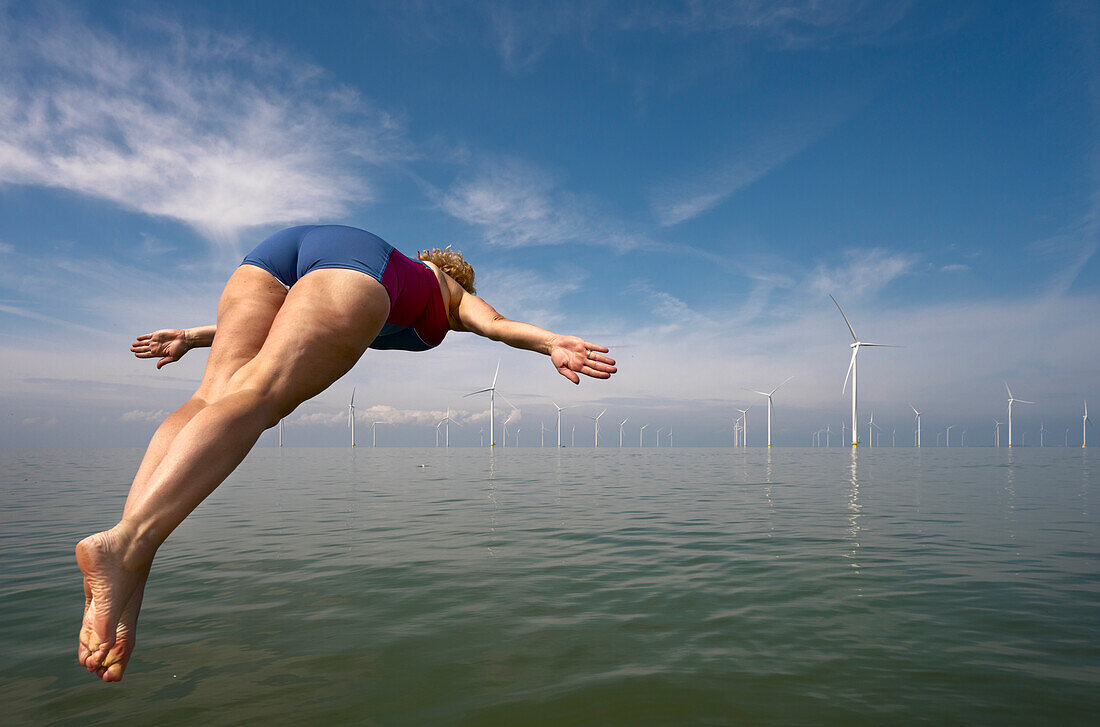 Netherlands, Friesland, Breezanddijk, Woman jumping into sea near wind turbines