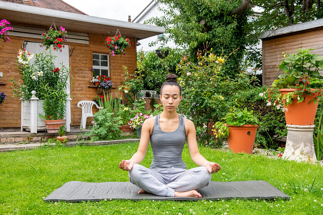 UK, London, Frau meditiert auf dem Rasen vor dem Haus
