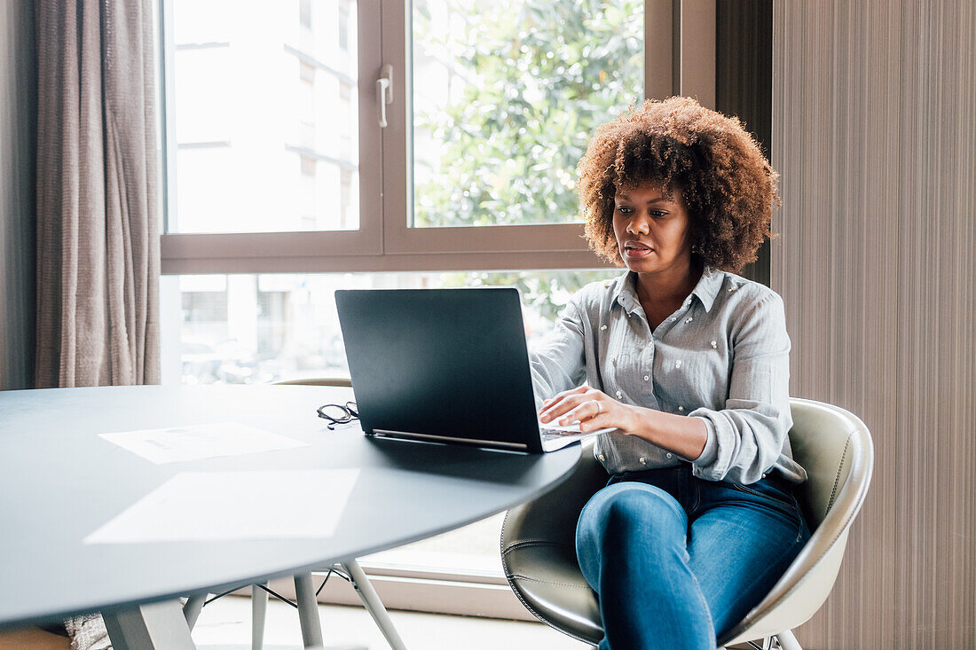 Italy, Businesswoman using laptop at table in creative studio