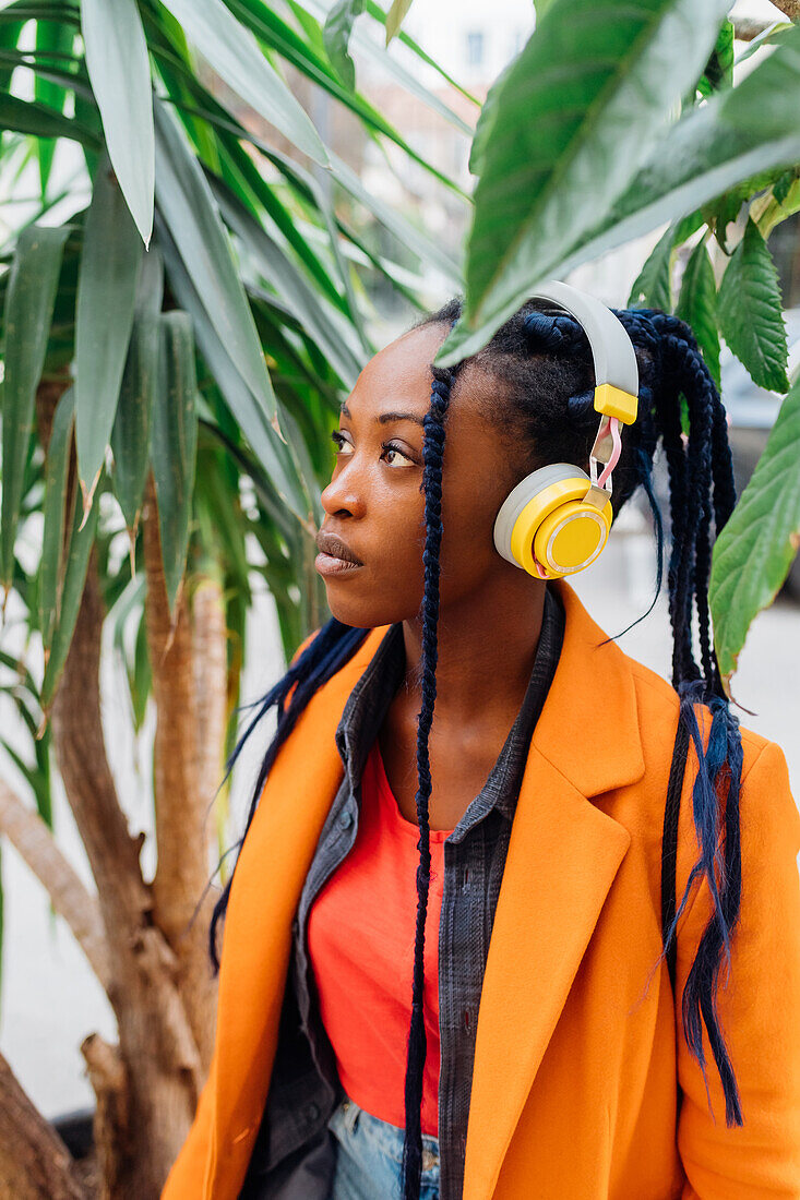 Italy, Milan, Woman with headphones surrounded with leaves