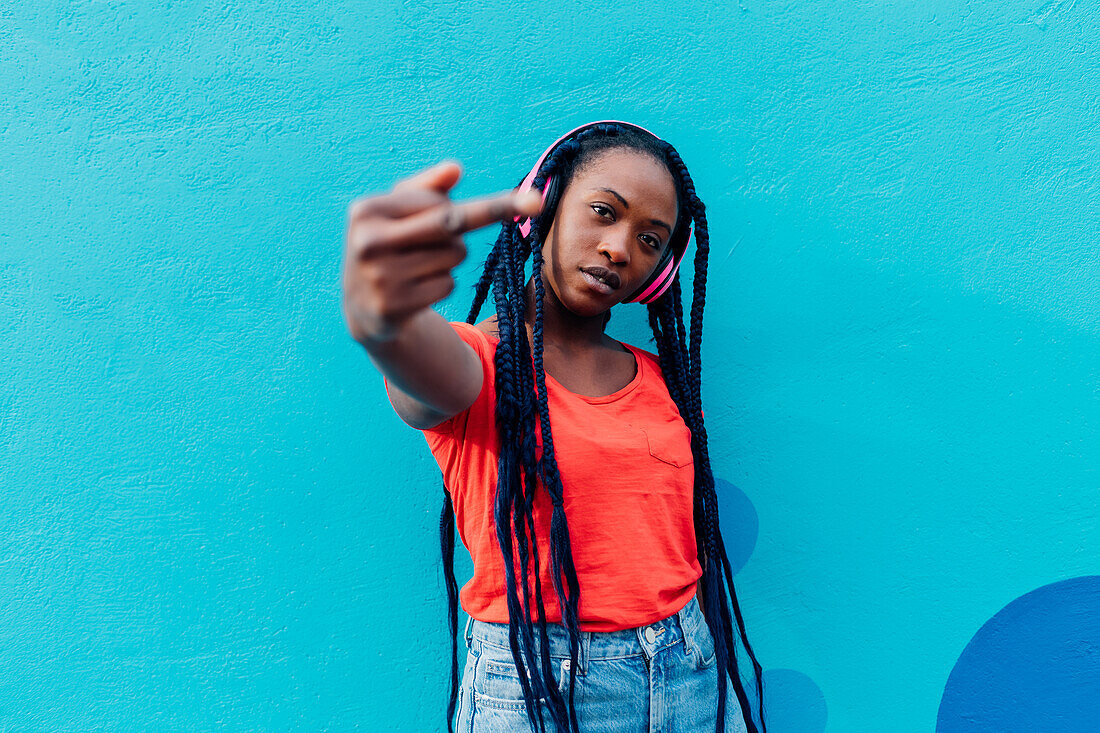 Italy, Milan, Young woman with headphones gesturing in front of blue wall